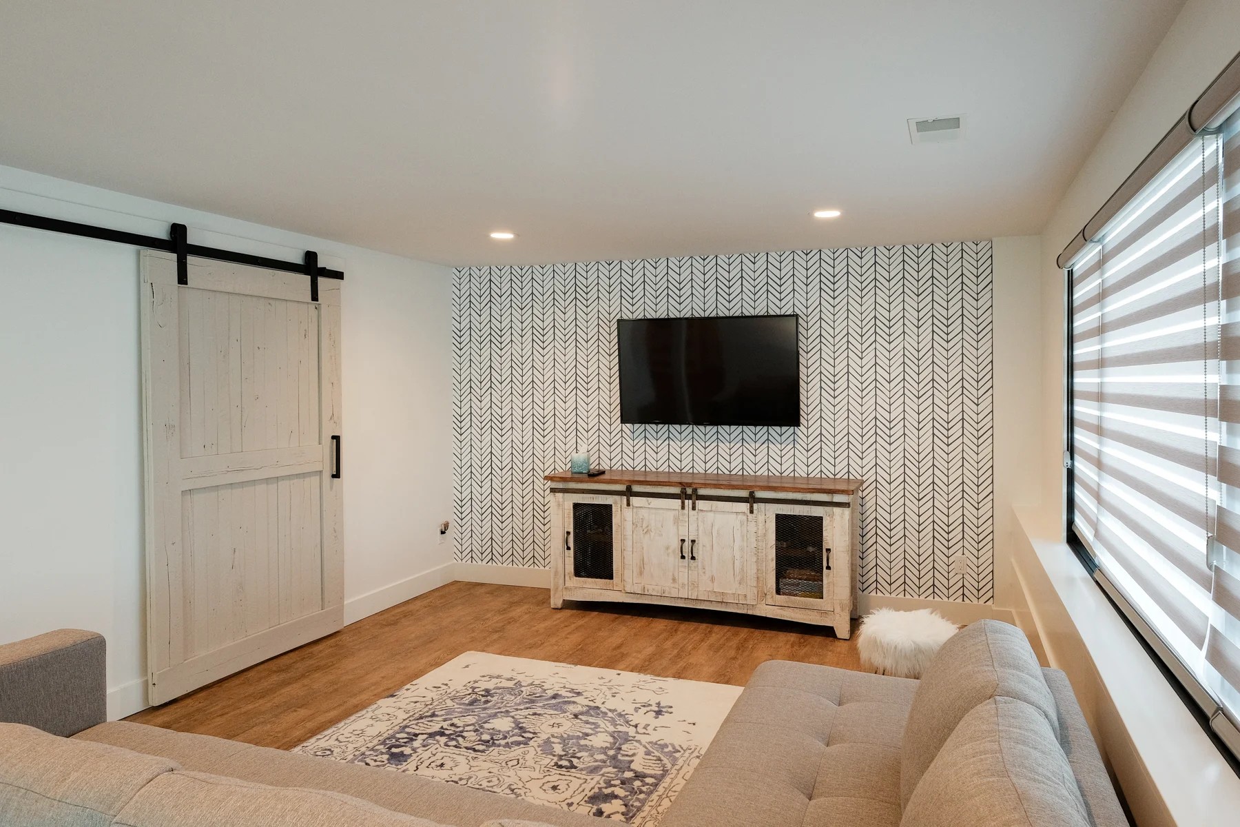 A renovated media room with a white shiplap barn door, a navy herringbone painted accent wall, a rustic media console, and oak floors.