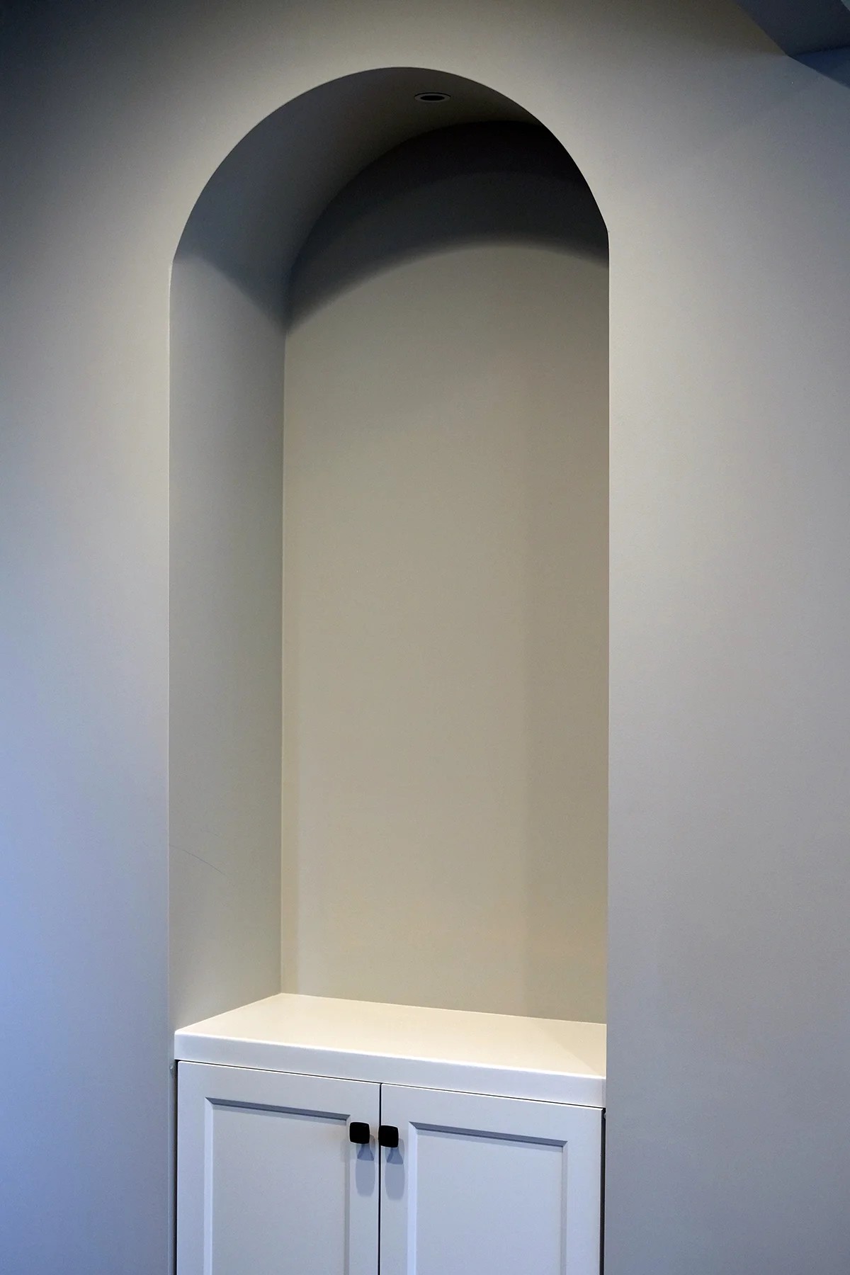 A custom arched plaster niche above a white shaker base cabinet with black hardware — architectural millwork built for the home.