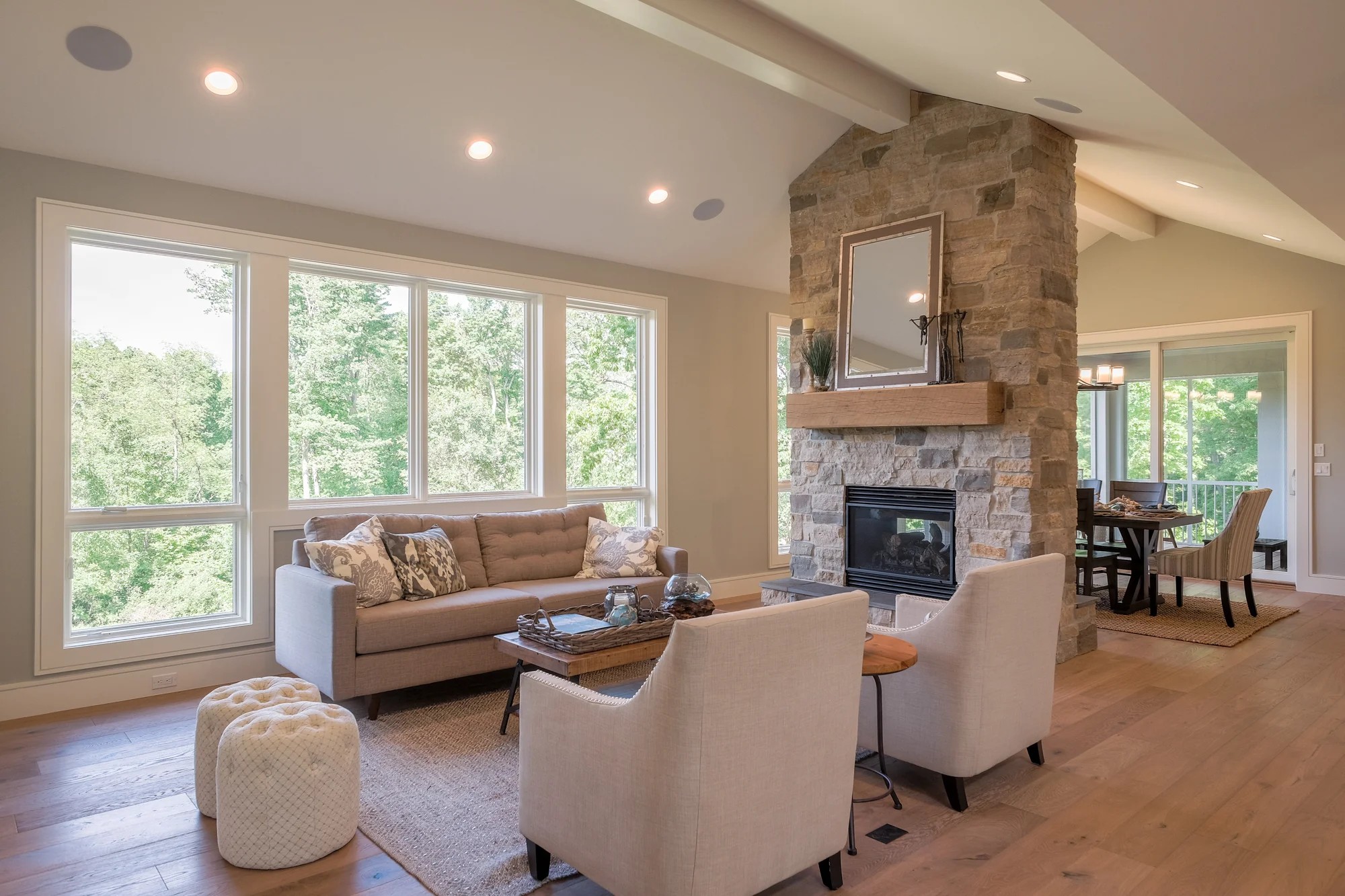 A great room with a stacked-stone fireplace, a vaulted ceiling, and a wall of windows, open to the dining area.