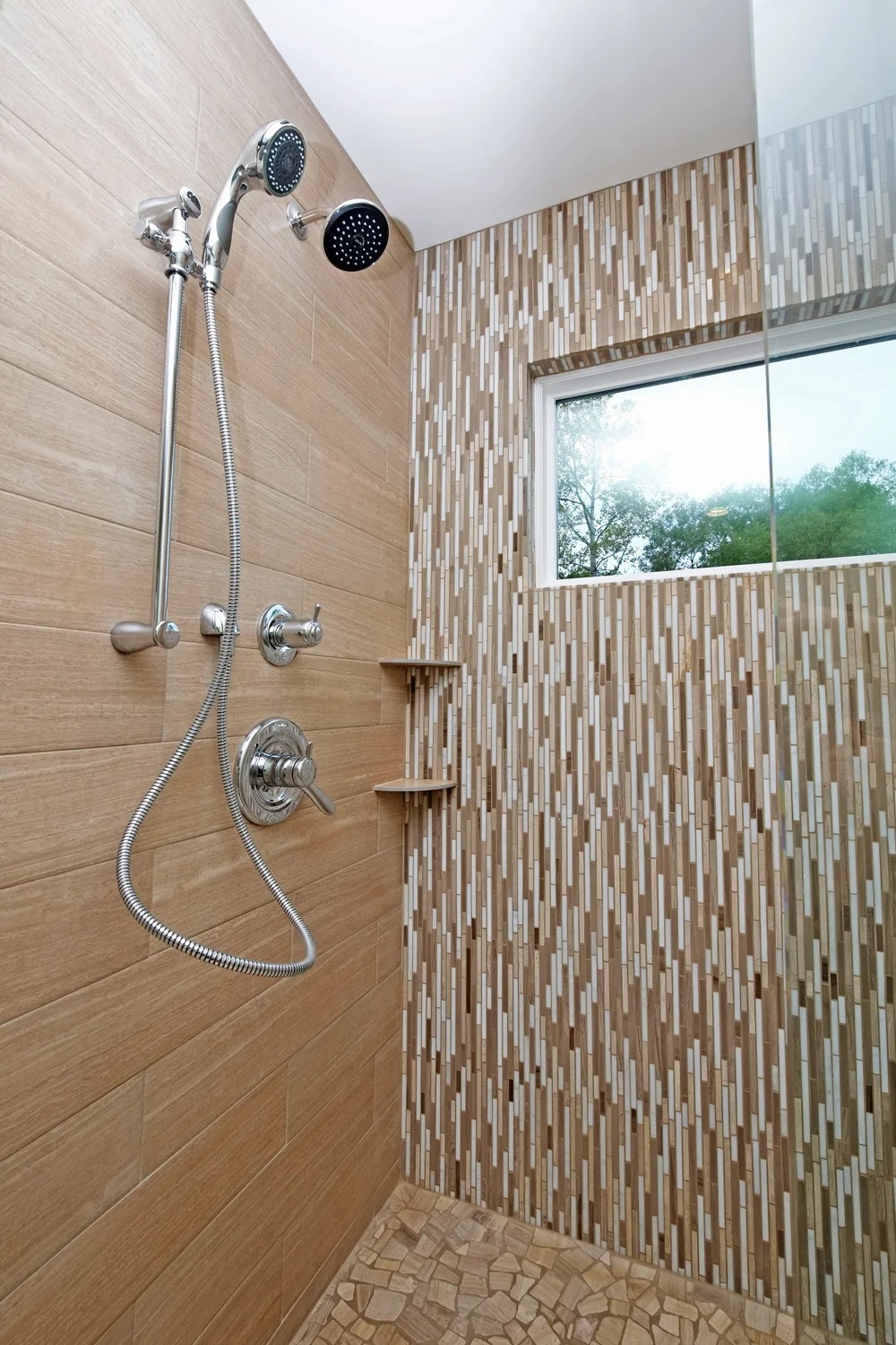 A walk-in tiled shower with a linear glass-mosaic accent wall, chrome fixtures, and a window.