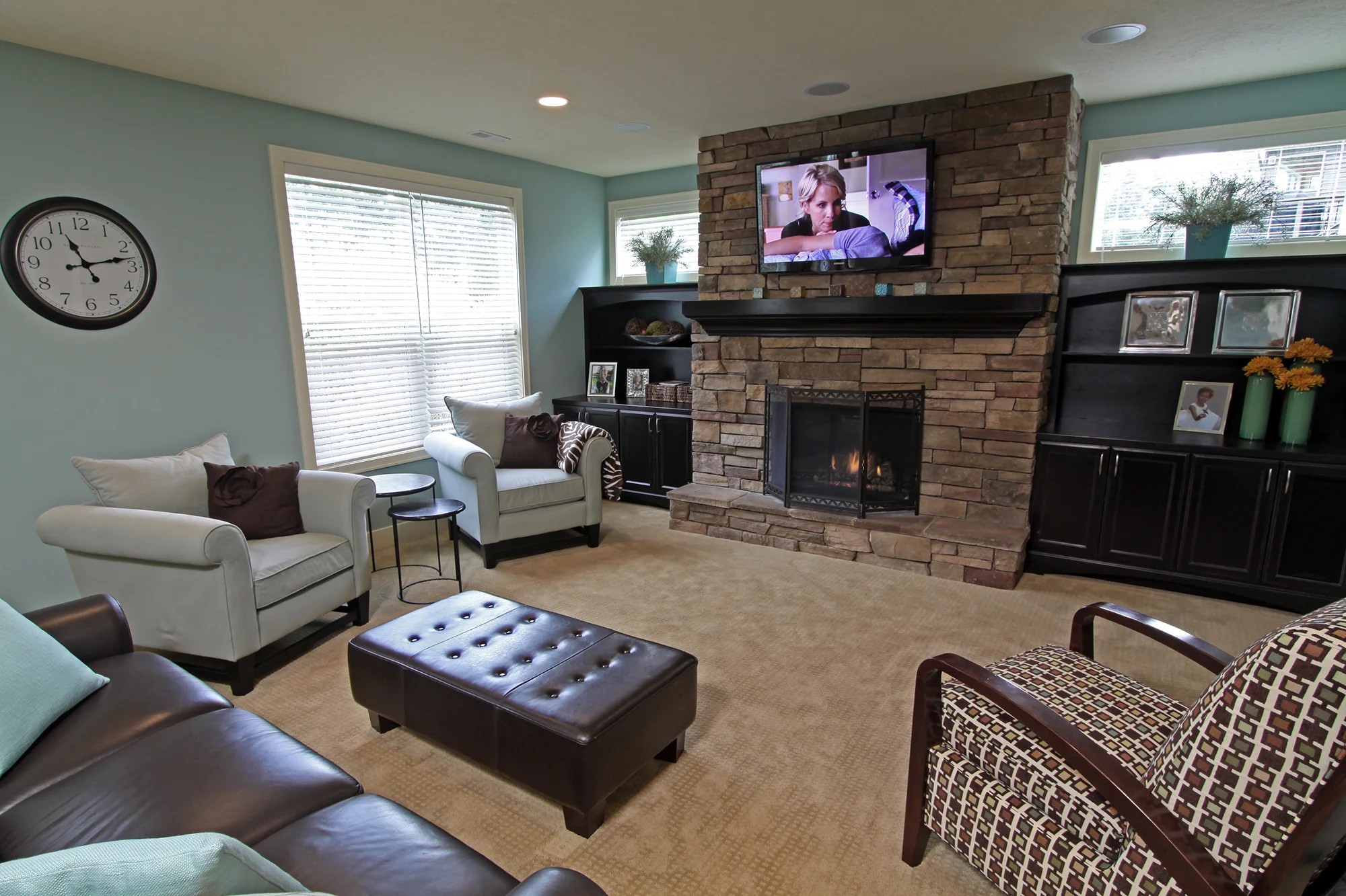 A finished lower-level family room with a stacked-stone fireplace, dark built-ins, teal walls, and a leather sofa.